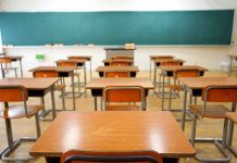 Classroom with wooden desks and empty green chalkboard.