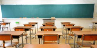 Classroom with wooden desks and empty green chalkboard.