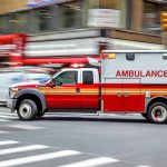 Red ambulance speeding through city intersection.