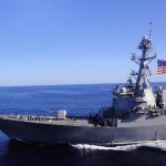 Warship sailing with American flag in open sea.