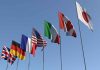 Flags of seven countries against clear blue sky.