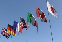 Flags of seven countries against clear blue sky.