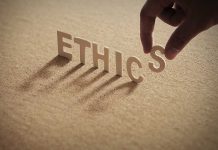 Hand placing the letter "S" in the word "ETHICS".