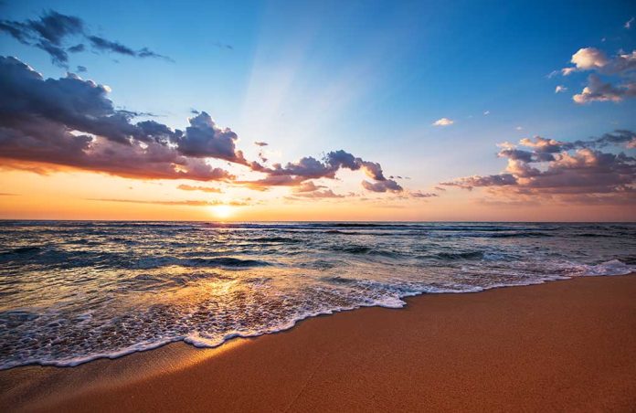 1196505853 featured image Sunset over a beach with waves and clouds.