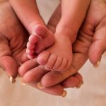 Adult hands holding newborn baby feet