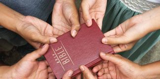 Hands holding a closed red Bible together