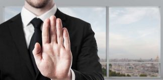 Person in suit with hand raised in stop gesture.