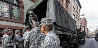 Soldiers gather around a military truck on street.