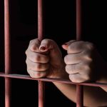 Hands gripping metal prison bars tightly