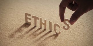 Hand placing the letter S in the word ETHICS