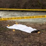 Crime scene by river with covered body and markers