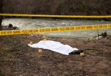 Crime scene by river with covered body and markers