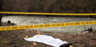 Crime scene by river with covered body and markers