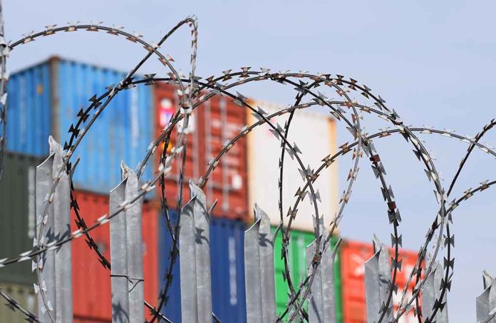 1377286811 featured image Barbed wire fence with shipping containers in background.
