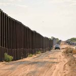 Border fence with vehicles on dirt road