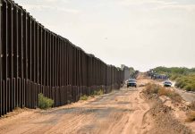 Border fence with vehicles on dirt road