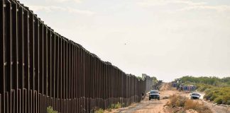 Border fence with vehicles on dirt road