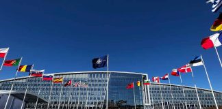 Flags outside NATO headquarters building under clear blue sky