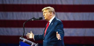 Person speaking at a podium with flag background