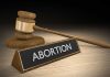 Gavel and sign reading "Abortion" on a wooden surface.