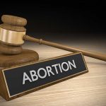 Gavel and sign reading "Abortion" on a wooden surface.