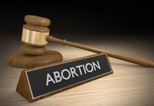 Gavel and sign reading "Abortion" on a wooden surface.