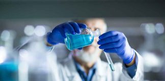 Scientist pouring blue liquid into test tube.