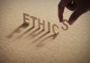 Hand placing the letter S in the word ETHICS
