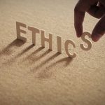 Hand placing the letter S in the word ETHICS