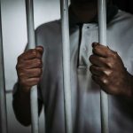 Person holding jail cell bars tightly