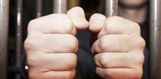 Hands gripping jail cell bars tightly
