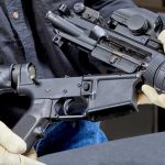 Person assembling a black rifle with gloves on