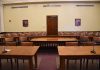Empty courtroom with wooden tables chairs and a door