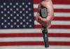 Hand holding gun with American flag background