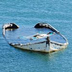 Half submerged weathered abandoned boat floating on calm water