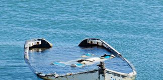 Half submerged weathered abandoned boat floating on calm water