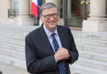 Man in suit outside building, flag in background.