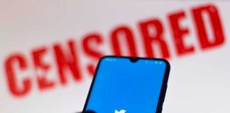 Phone displaying Twitter app with CENSORED in background