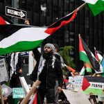 Protesters with flags and signs, one holding a megaphone