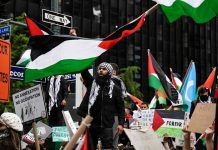 Protesters with flags and signs, one holding a megaphone