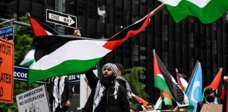 Protesters with flags and signs, one holding a megaphone