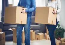 Two people carrying cardboard boxes indoors.