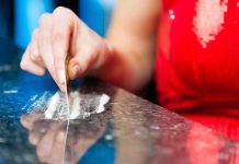A hand using a card to prepare a line of white powder on a reflective surface