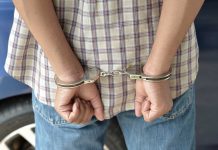 A person in handcuffs viewed from behind wearing a plaid shirt and denim jeans
