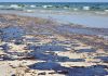 Oil spill on a sandy beach with waves in the background