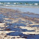 Oil spill on a sandy beach with waves in the background