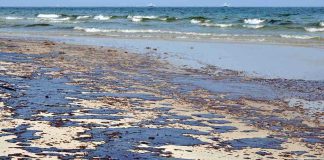 Oil spill on a sandy beach with waves in the background