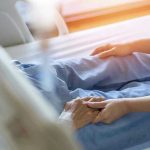 Hospital patient holding visitor's hand reassuringly.