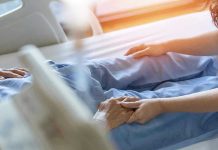 Hospital patient holding visitor's hand reassuringly.