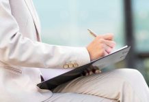 Person in beige suit writing on a clipboard